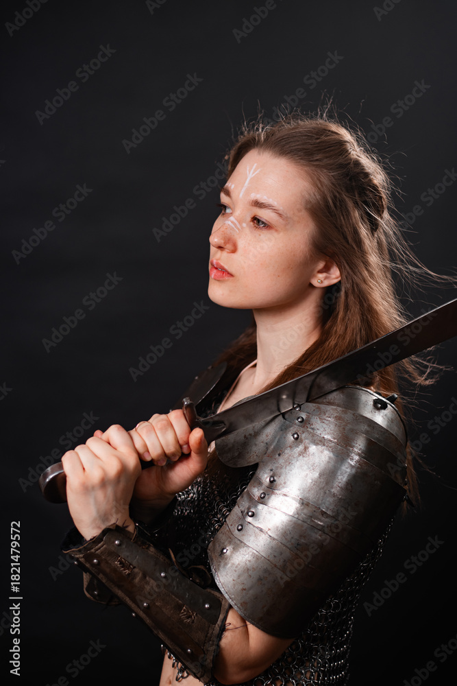 Obraz premium Portrait of a young woman, fantasy warrior in armor with a sword in her hands isolated on a dark background.
