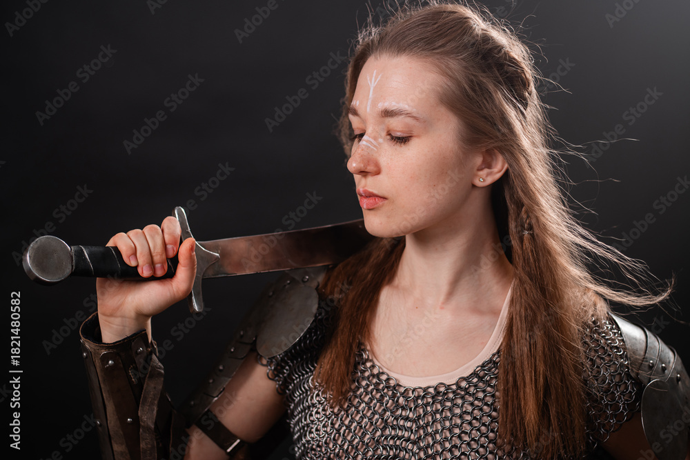 Fototapeta premium Portrait of a young woman, fantasy warrior in armor with a sword in her hands isolated on a dark background.