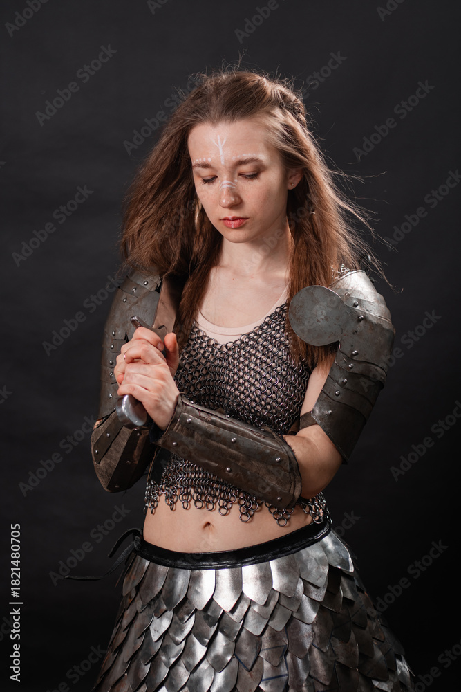 Fototapeta premium Portrait of a young woman, fantasy warrior in armor with a sword in her hands isolated on a dark background.
