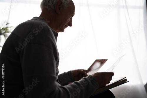 Slika na platnu Senior sad man looking old photo missing his wife sitting on sofa at home