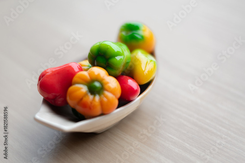 Colorful Thai mung bean desserts (look choop) shaped like mini fruits and vegetables, displayed beautifully in a small ceramic plate on a wooden table. Traditional Thai sweet.