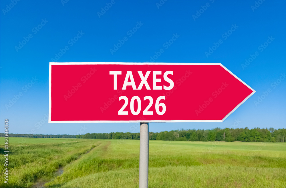 Obraz premium Taxes 2026 new year symbol. Concept words Taxes 2026 on beautiful red road sign. Beautiful green grass field forest and blue sky background. Business and taxes 2026 new year concept. Copy space.