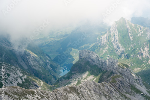 A stunning panoramic view of rugged Swiss Alps mountains in Appenzell partially covered by low-hanging clouds and fog.