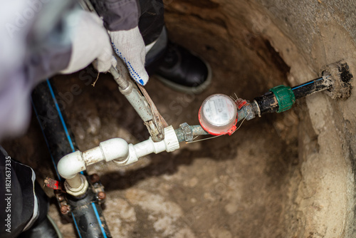 A plumber tightens a threaded fitting on a pipe in a water well with an adjustable wrench. Plumbing repair and maintenance
