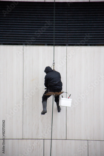 Vertical photo of industrial climber descending on ropes. The man hangs from safety lines on the wall of a building. Conceptual representation of dangerous work and hard labor