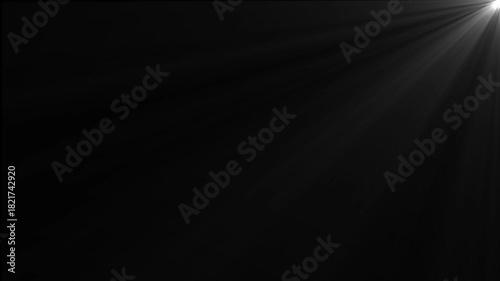 A single spotlight in the upper right corner casting bright rays of light downwards and left on a dark background