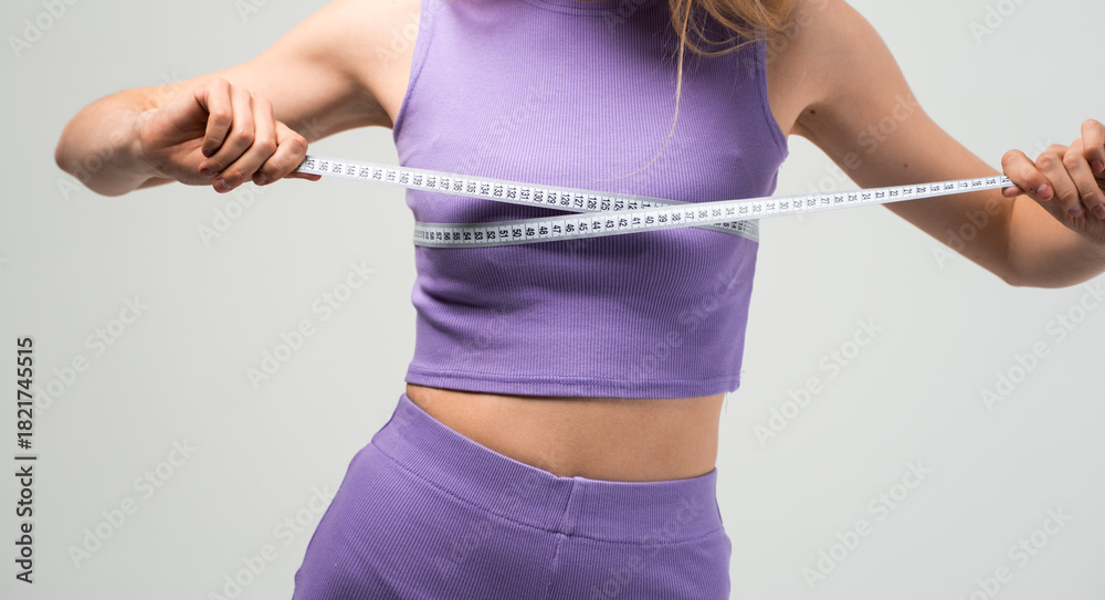 Fototapeta premium Woman measuring bust with tape in purple sportswear isolated on neutral background