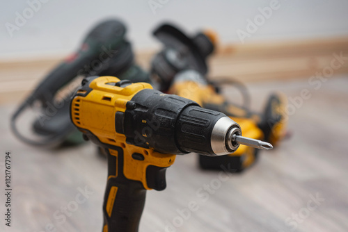 Yellow cordless drill with additional power tools in the background. Construction work, home improvement, mechanical tasks and modern workshop equipment.