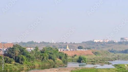 A peaceful riverside landscape featuring lush green fields, flowing water, and a clear blue sky. The natural scenery creates a calm and refreshing atmosphere.