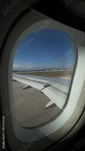 View from airplane window showing the wing as the plane taxis to the runway, preparing for takeoff with runway lights and airport surroundings visible
