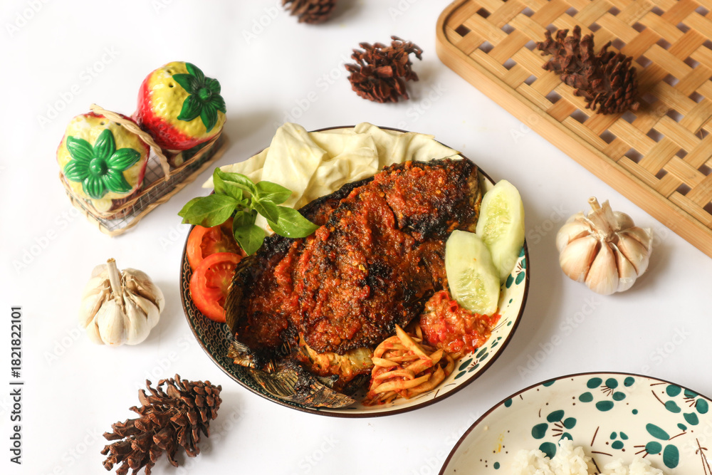 Φωτογραφία A plate of Indonesian-style spicy grilled tilapia, known as ikan bakar bumbu rujak, served with fresh raw vegetables, fiery sambal, and tangy mango relish called sambal mangga