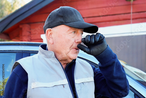 Tableau sur toile Work in pause — portrait of a mature man in cap and gloves, touching his face briefly during a moment of reflection or rest near vehicle