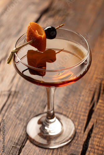 Old-fashioned cocktail with orange peel and cherry on a rustic dark wood table. 