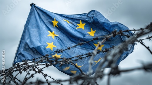 European Flag Waves Against a Backdrop of Barbed Wire, Symbolizing Confinement and Restriction in a Troubled Environment