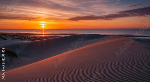Fototapeta Naklejka Na Ścianę i Meble -  Vibrant golden sunset over vast sandy beach dunes and tranquil ocean