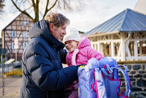 Little girl walking home from school with big bag. Her father meet her on the way. Walking together.