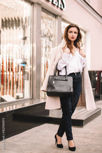 Elegant woman in stylish coat standing on city street with handbag