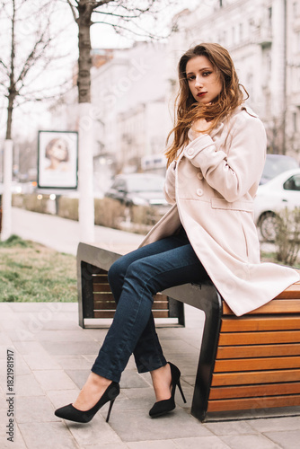 Elegant woman in stylish coat standing on city street with handbag