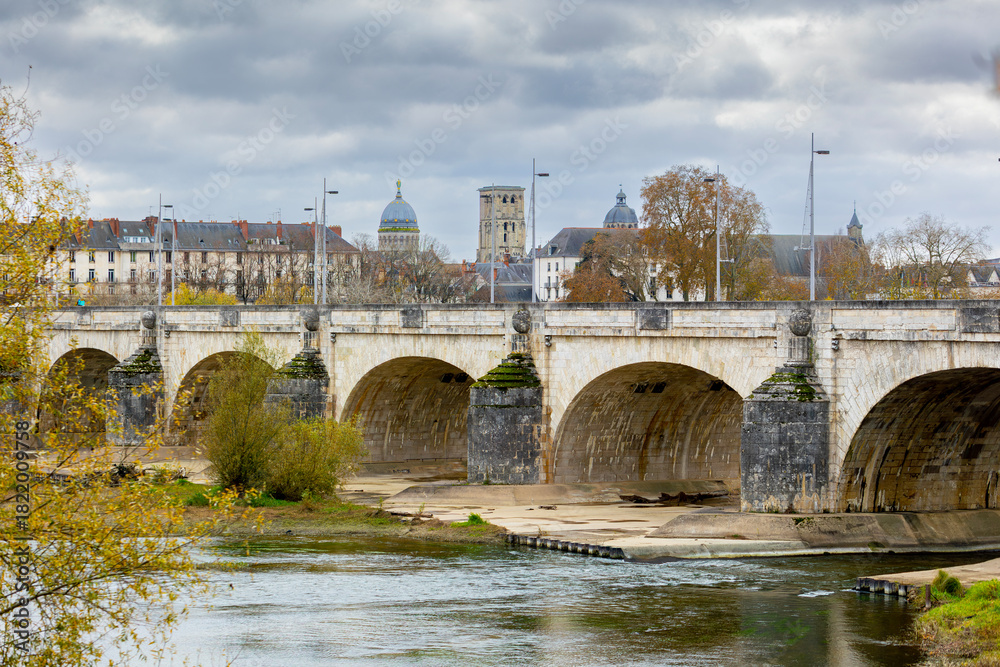 Naklejka premium Historic stone arched Wilson Bridge crosses the Loire River in Tours France with Saint Martin Basilica and Tour Charlemagne tower visible in the distance creating a beautiful city landscape view