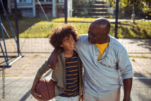 Mature father and teen son sharing supportive moment on basketball court