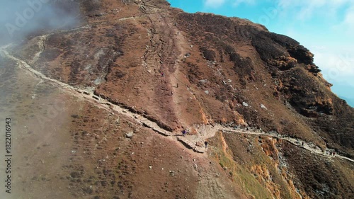 Aerial drone shot orbiting people devotees climbing narrow stair covered path of Tungnath Trek from Chopta to get to world's highest Shiv temple on barren stony mountains covered in clouds Uttarakhand