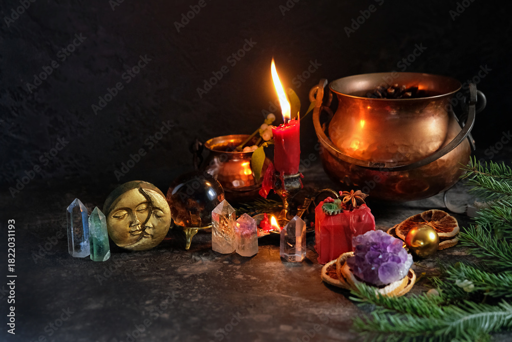 Naklejka premium Wiccan altar for Yule holiday. Burning candle, moon amulet, mineral gemstones, witch cauldrons, decor, fir branches on dark table. Crystal Ritual. witchcraft, magic ceremony for Yule, Winter Solstice