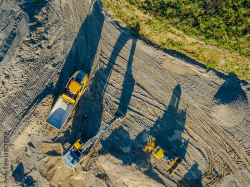 Aerial view of construction machinery in gravel pit. Dumper and excavator from above with long shadows.