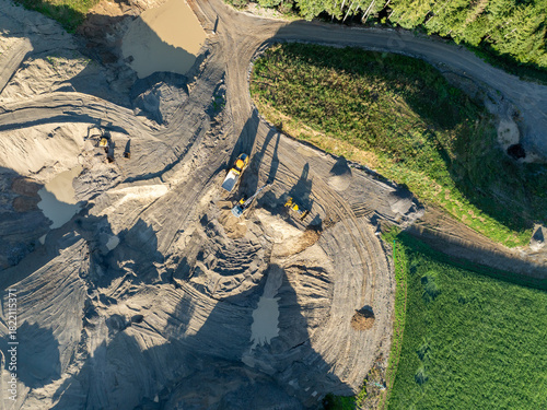 Aerial view of construction machinery in gravel pit. Dumper and excavator from above with long shadows.