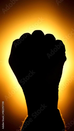 Human hand forming a fist in silhouette against a golden glow.