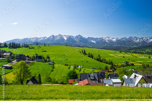 Fototapeta Naklejka Na Ścianę i Meble -  Panoramic view of the snow-capped Tatra Mountains from Rzepiska village in Podhale, Poland. Scenic June landscape with vivid green fields and rural settlement.