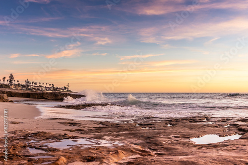 Obraz na plátně Beautiful scene of wave crashing on rocks in front of beach homes in La Jolla Ca