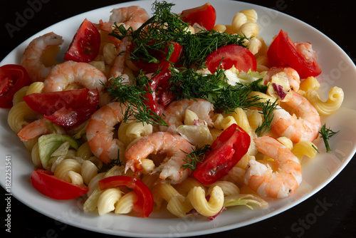 Pasta with shrimp, vegetables and herbs on a plate on a black background