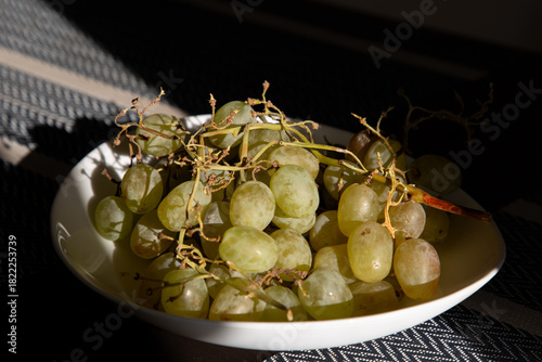 A white plate with grapes on the table illuminated by sunlight