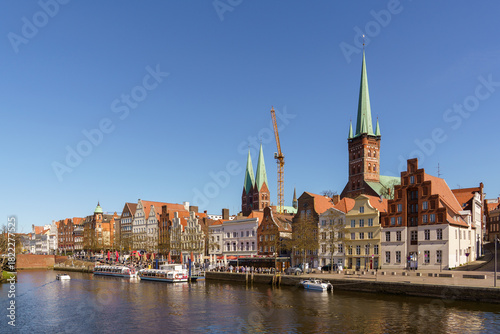Fototapeta Naklejka Na Ścianę i Meble -  A panoramic view of houses on the waterfront in Lubeck, Germany The dock accommodates many small boats and ships. The weather is sunny and clear, with a blue sky