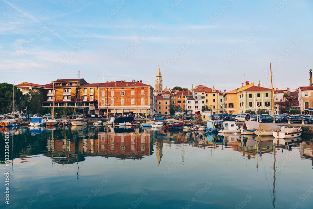 Fototapeta premium Harborfront Panorama of Izola with Reflections of Boats and Historic Architecture