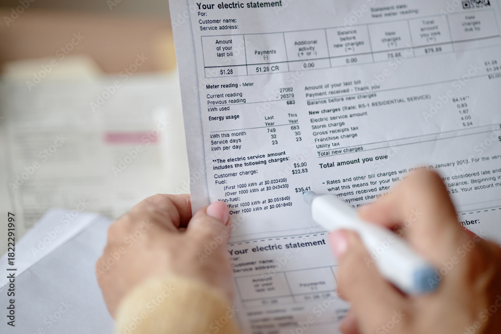 Naklejka premium Adult woman holding pen reviewing utility bill and invoice documents at desk, focusing on analyzing charges and payment details, hands in close up