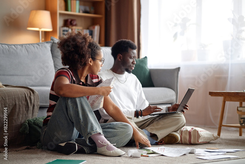 Canvas-taulu Young Black man using laptop while young Black woman analyzing invoices and bill