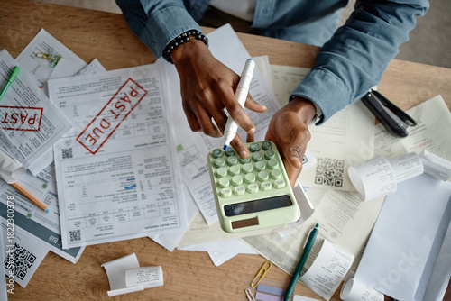 фотографія Black man using calculator and pen while analyzing invoices and bills on clutter