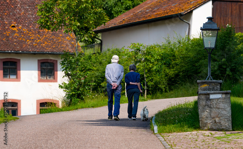 An elderly European couple (man and woman) walks in nature with a dog. Senior couple shares a joyful moment, with copy space. It suggests a comfortable and happy relationship. Switzerland.