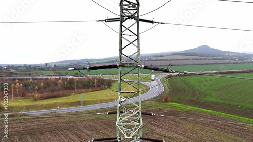 Aerial drone view of power transmission lines stretching across open terrain, tall pylons and cables forming strong linear patterns that highlight energy distribution and industrial landscape.