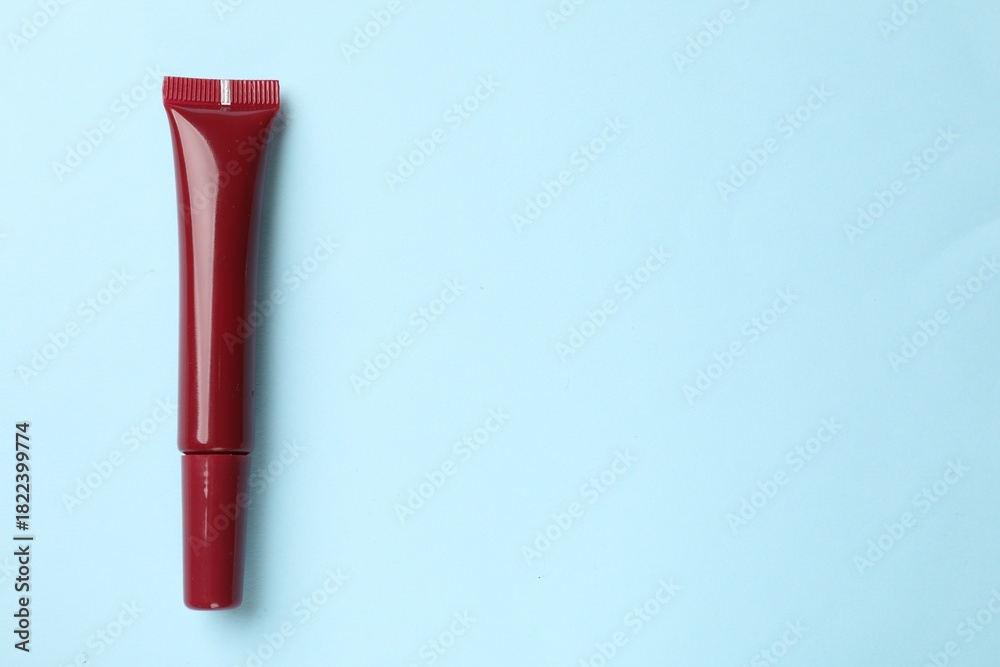 Obraz premium Beautiful dark red lip gloss on light blue background, top view. Space for text