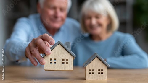 Smiling senior couple comparing two miniature wooden house models on table