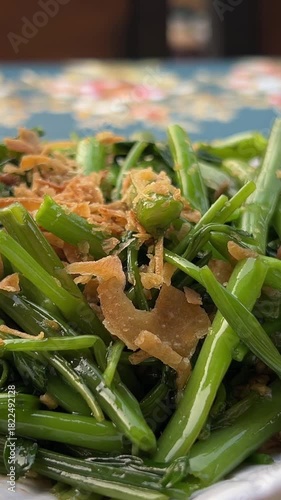 Close-up of chopsticks grabbing stir-fried water spinach greens in savory sauce from a white plate. Ideal for Asian cuisine, vegetarian dishes, and dining themes.