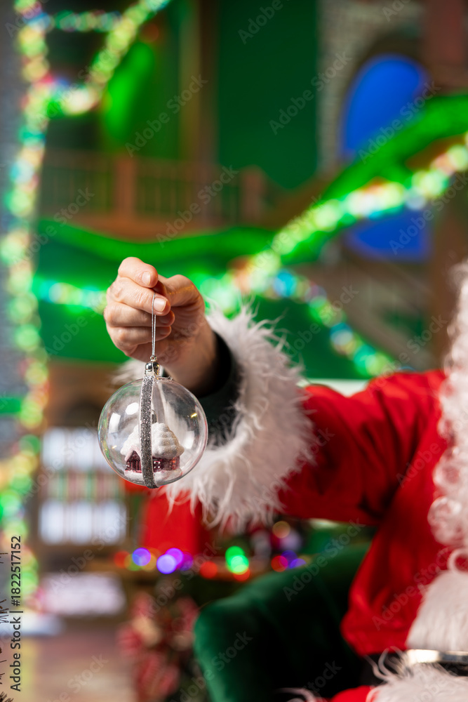 Naklejka premium Close up of entertainer wearing red xmas suit holding Christmas prop, doing festive decorations for holiday season ambiance. Santa Claus using globes to decorate room during December festivities