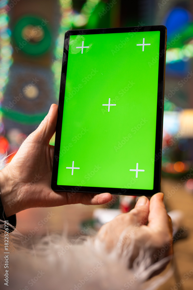 Obraz premium Close up of Santa Claus using mockup digital tablet to check naughty and nice kids list. Santa analyzes children behavior, preparing gifts for good children using green screen touchscreen device