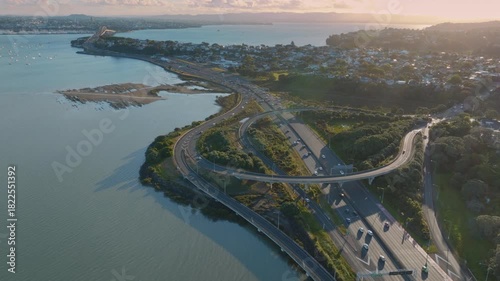 Aerial view of Northcote, Auckland, New Zealand, showing the Harbour Bridge and motorway. Cars are traveling along the highway, connecting different parts of the city.