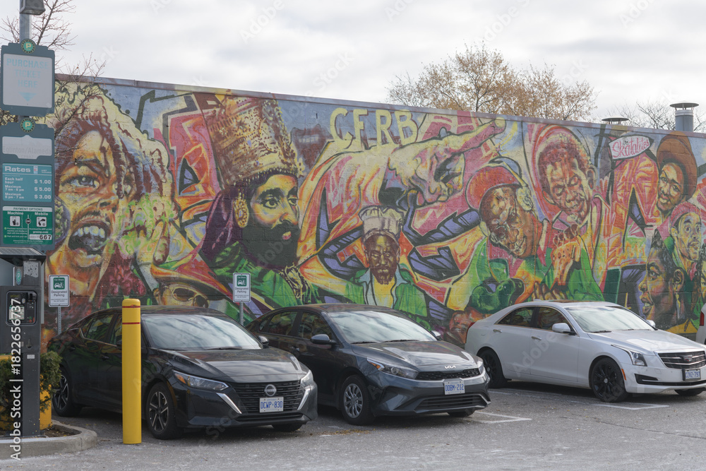 Naklejka premium Green P, a parking lot, (Municipal Carpark 667), located at 1531 Eglinton Av W, with cars and Reggae Lane Mural by artist Adrian Hayles, Little Jamaica, Toronto