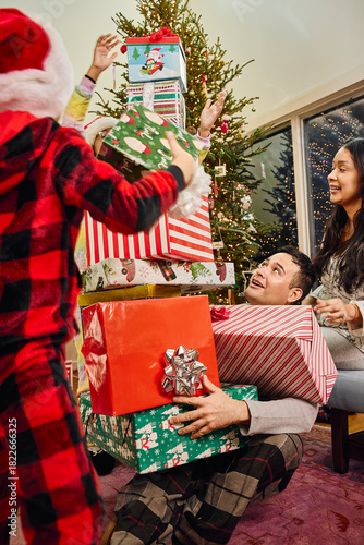 Family celebrates Christmas morning with stacked wrapped presents near decorated tree at home