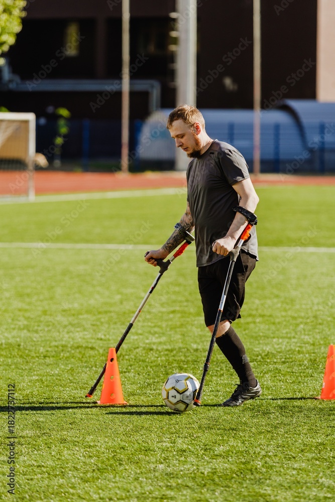 Obraz premium Man on crutches walking towards ball near cone