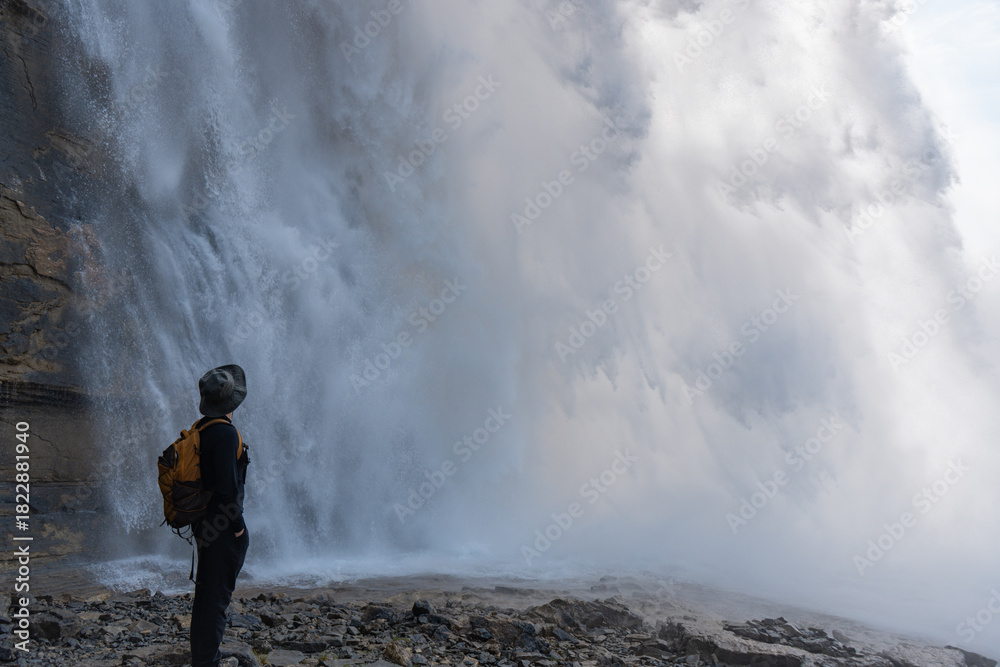Obraz premium A hiker marvels at the grand, misty waterfall. The power of nature visible.